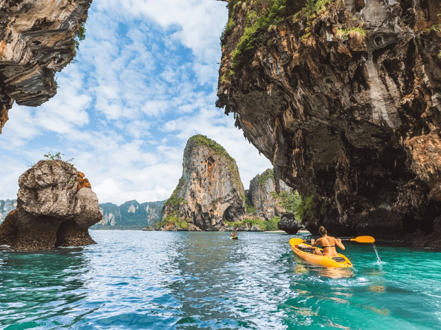 a woman paddles a kayak past rocky islands