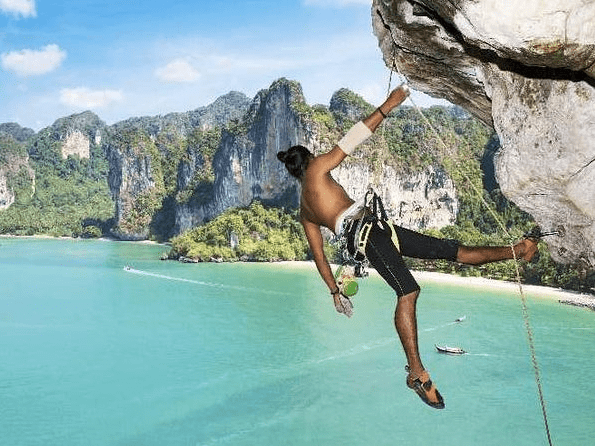 man in rock climbing gear hangs from a cliff with view to coastal bay