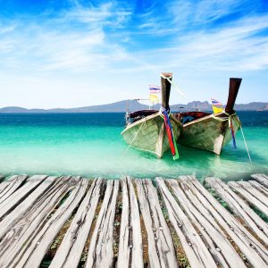 two wooden boats moored at a rustic wooden jetty under a blue sky
